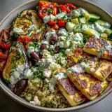 A beautifully arranged Mediterranean bowl featuring grilled halloumi, smoky eggplant, and quinoa topped with tzatziki. Perfect for a vibrant, healthy lunch. 