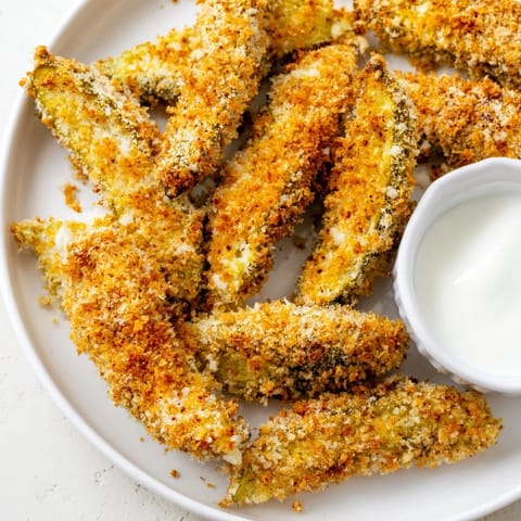 Golden-brown Fried Pickles stacked on a plate with a small bowl of creamy ranch dressing for dipping.