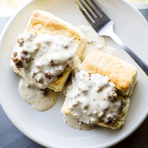 Golden, flaky biscuits split open and generously smothered in creamy, peppery sausage gravy, ready to serve for a hearty Southern breakfast.