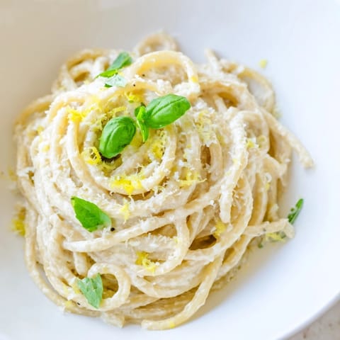 Lemon ricotta pasta served in a white bowl, garnished with black pepper and Parmesan, with a glass of crisp white wine nearby.