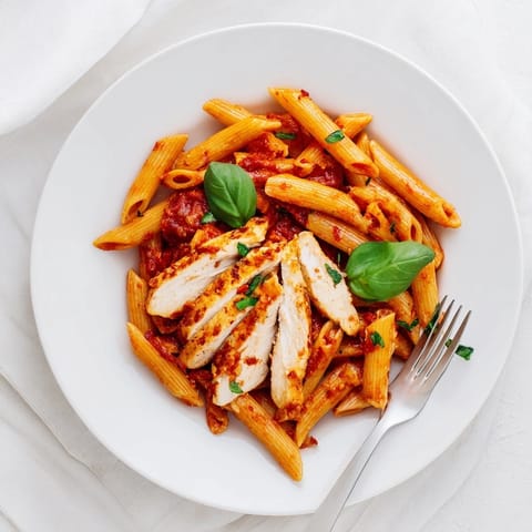 Overhead view of hearty spicy tomato chicken pasta featuring golden-brown chicken, al dente penne, and vibrant red sauce on a rustic plate.