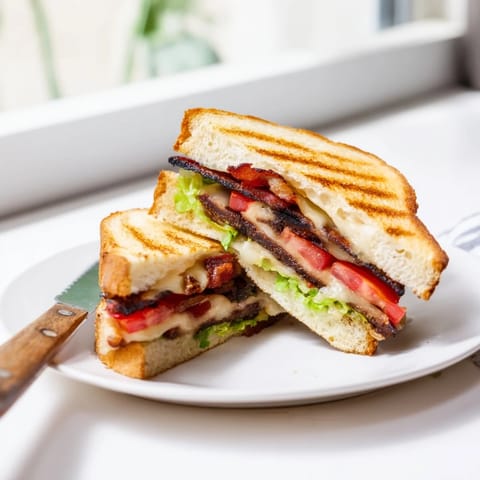 A close-up of a Vegan Bacon BLT Grilled Cheese, with golden, buttery sourdough bread cradling melted vegan cheese, smoky tempeh bacon, crisp romaine lettuce, and ripe tomato slices.