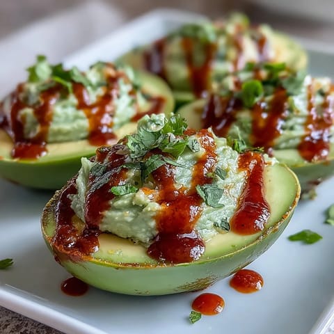 Creamy avocado deviled eggs with Sriracha drizzle, a spicy twist on a classic appetizer.  